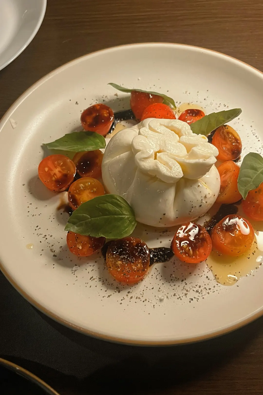 Burrata cremosa servida com tomates confit, folhas de manjericão fresco e fio de azeite